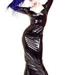 Fourth pic of Alt model Darenzia in long black latex dress and platform shoes poses with big gun