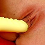 Third pic of Smiling blonde drills her tight pussy with a yellow toy on a red bed - IamXXX.com