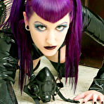Second pic of Flirtatious Natalie Addams with purple hair and smooth pussy poses in black latex outfit