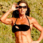 Third pic of Bodybuilder Lynnie Brooks poses on sandy ground in a bikini and sunglasses