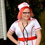 Fourth pic of Thick redhead removes leather attire to pose nude before donning nurse garb