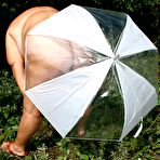 Second pic of Obese oma Grandma Libby holds an umbrella while posing naked by fir trees
