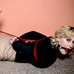 Second pic of Clothed woman with blonde hair sports a ball gag in mouth while hogtied